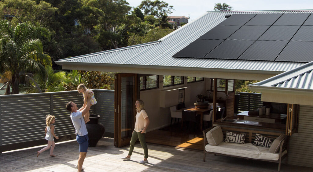 Happy family playing in their backyard with solar panels seen on the roof